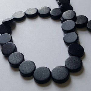 May include: A strand of black wooden beads, each bead is round and flat, arranged in a circle.