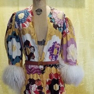 May include: A long, patchwork robe with a V-neckline and long sleeves. The robe is made of various fabrics in shades of red, blue, yellow, and purple. The sleeves have white fur cuffs. The robe is cinched at the waist with a brown belt.