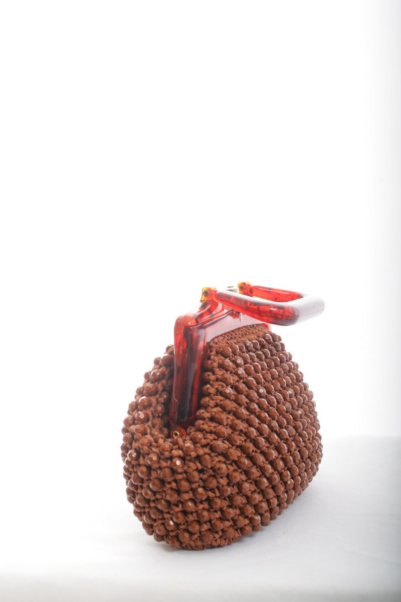May include: A brown beaded purse with a red plastic handle. The purse is made of small, round beads that are woven together.