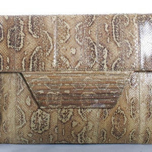 May include: A brown snakeskin clutch purse with a flap closure and a textured design.