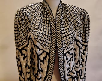 May include: A black and white sequined jacket with a geometric pattern. The jacket has a V-neck and long sleeves.
