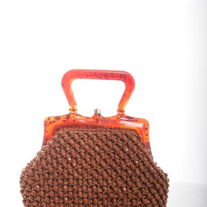 May include: A brown beaded purse with a clear orange plastic handle and clasp.