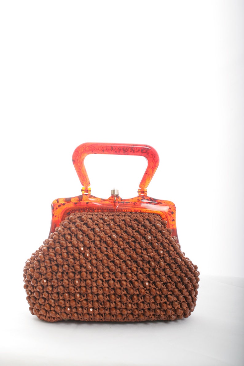 May include: A brown beaded purse with a clear orange plastic handle and clasp.