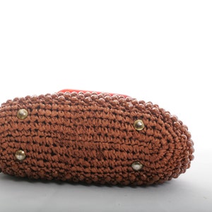 May include: A brown woven handbag with a rounded shape and gold accents. The bag is made of a woven material and has a smooth texture.
