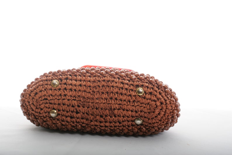 May include: A brown woven handbag with a rounded shape and gold accents. The bag is made of a woven material and has a smooth texture.