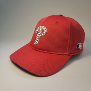 May include: Red baseball cap with a white rhinestone 'P' on the front and a blue and white MLB logo on the side.