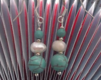 Op de afbeelding: Hangende oorbellen met turquoise, parel en zilveren kralen. De oorbellen hebben een haaksluiting en een gelaagd ontwerp. De onderste kraal is een grote turquoise bol, met een parel in het midden en een kleine turquoise kraal aan de bovenkant.