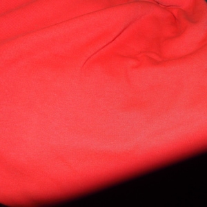 May include: A close-up of a bright red fabric with a smooth, even texture. The fabric is slightly wrinkled and has a subtle sheen.