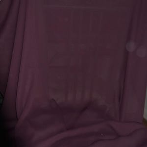 Pode incluir: Um fundo de tecido roxo escuro com uma superfície lisa e sem rugas. O tecido é drapeado e dobrado, criando linhas suaves e fluidas.