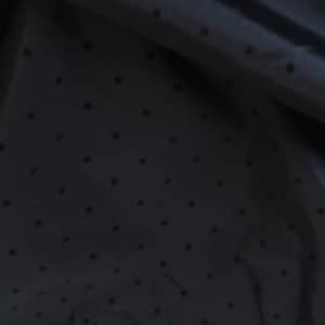 May include: Close-up of a black fabric with a subtle polka dot pattern. The fabric has a smooth, slightly shiny texture.