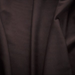 Puede incluir: Un primer plano de una tela marrón oscura con pliegues y arrugas suaves. La tela tiene una textura suave y sedosa.