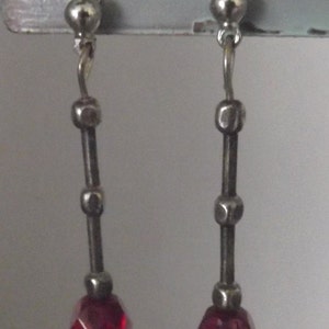 May include: A pair of silver dangle earrings with red faceted glass beads at the bottom.