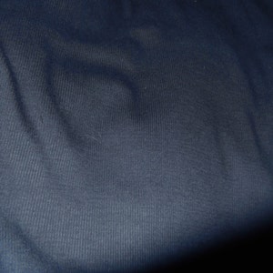 May include: Close-up of a navy blue fabric with a ribbed texture. The fabric has a slight sheen and appears to be soft. The image is well-lit, highlighting the texture and color of the material.