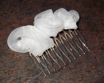 May include: A white tulle hair comb with a silver metal comb. The tulle is arranged in a flower shape.