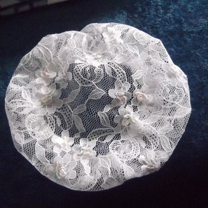 May include: White lace hair covering with floral design and pearl-like embellishments.