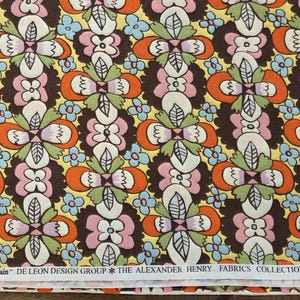 Könnte beinhalten: Stoff mit einem sich wiederholenden Blumenmuster in Braun, Orange, Rosa, Weiß, Grün und Blau. Das Design umfasst stilisierte Blumen und Blätter auf gelbem Hintergrund. Der Text "eden chain" und "DE LEON DESIGN GROUP" ist sichtbar.