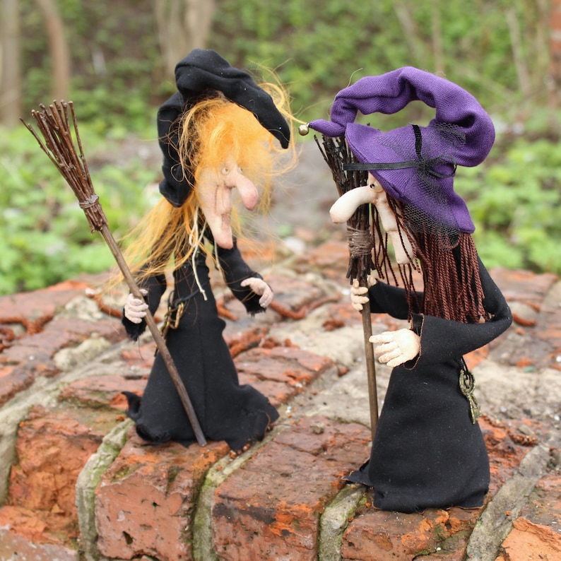 May include: Two handmade witch dolls with long black robes, purple and black hats, and broomsticks. The dolls have long hair, one with blonde hair and the other with brown hair.