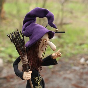 May include: A purple witch hat with a bell on top, a brown broom, and a witch doll with a long nose and brown hair.