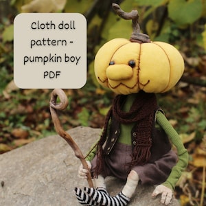 May include: A handmade cloth doll with a pumpkin head, wearing a green shirt, brown vest, and shorts. The doll has a brown scarf and is holding a wooden stick. The text on the image says "Cloth doll pattern - pumpkin boy PDF".