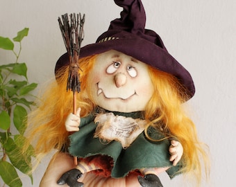 May include: A handmade Halloween witch doll with orange hair, a purple hat, and a green dress. The doll holds a small broom and has a whimsical, smiling face. The doll's features are hand-painted, and it has black shoes.