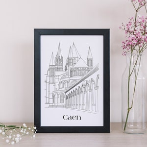 Può includere: Una stampa incorniciata nera di un disegno a linea di un edificio con la parola "Caen" stampata sotto l'immagine.