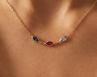 May include: A delicate gold chain necklace featuring three marquise-cut gemstones arranged horizontally. The stones are set in gold bezels and include a deep blue sapphire, a vibrant red ruby, and a light blue aquamarine, creating a colorful accent.