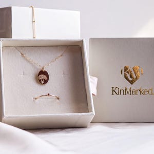 a jewelry box with a necklace and a pendant, as well as a box with the brand name "KinMarked" printed on it.