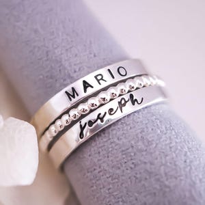A silver ring with the name "MARIO" engraved on it, placed on a textured gray surface.
