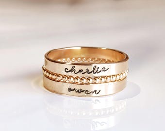 May include: A stack of three gold-toned rings. The top ring is smooth, the middle ring features a beaded texture, and the bottom ring is smooth. The top ring is engraved with the name charlie and the bottom ring is engraved with the name owen.