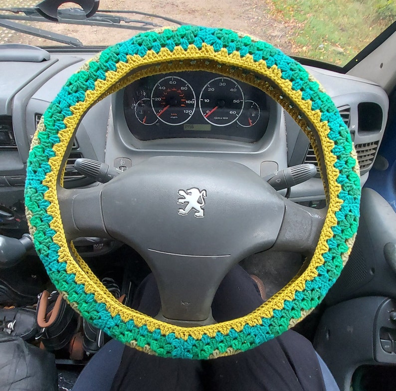A crochet granny Square steering wheel cover, in light green,khaki green, forest green, dark green and teal blue.