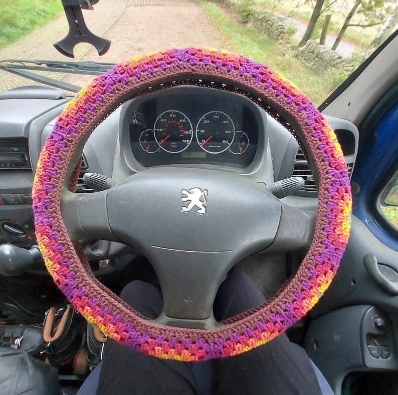 A bohemian style steering wheel cover. In colours from the centre to the outside, green,yellow,orange,red,purple and brown.