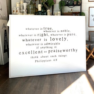 May include: White wooden sign with black text that reads "whatever is true, whatever is noble, whatever is right, whatever is pure, whatever is lovely, whatever is admirable if anything is excellent or praiseworthy think about such things. Philippians 4:8"