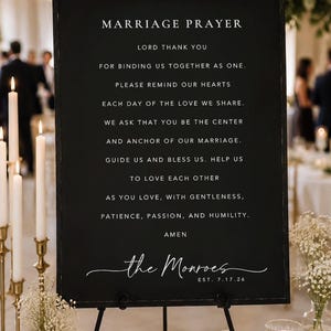 May include: A black sign with white text, displayed on a black easel. The sign reads "Marriage Prayer" followed by a prayer. The bottom of the sign has the names "the Monroes" and the date "EST. 7.17.26".