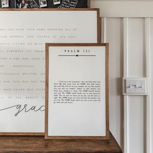 May include: A white wooden sign with the text "PSALM 121" in black lettering. The sign features a black line above the text and a black diamond below the text. The sign also includes a passage from Psalm 121 in black text.