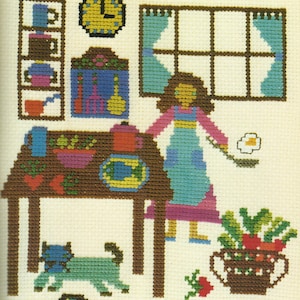 Può includere: Uno schema di punto croce che rappresenta una scena di cucina con una donna che cucina, un gatto, un tavolo con del cibo e un orologio al muro.