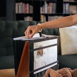May include: A black and brown leather folder with a white sheet of paper inside. The folder is open and has several compartments. The paper has a knitting pattern on it with the title "Daisy Daisy".