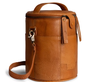 May include: A cylindrical, brown leather wine carrier with a top handle and a detachable shoulder strap. The bag has a zippered top, a side pocket, and a leather tag with the word "muud".