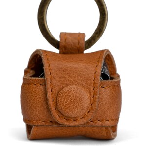 May include: A brown leather keychain with a metal ring. The keychain has a flap with a button closure.