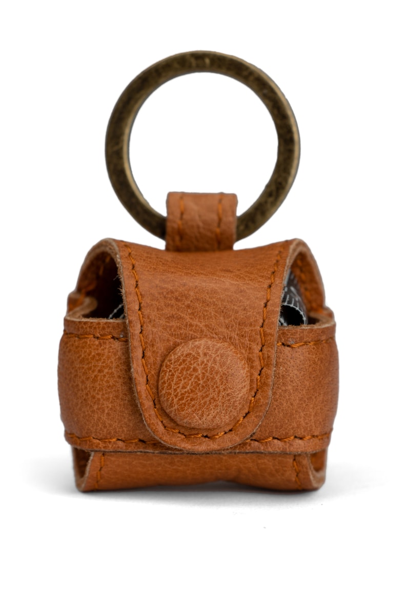 May include: A brown leather keychain with a metal ring. The keychain has a flap with a button closure.