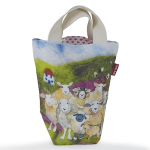 May include: A tote bag with a whimsical sheep illustration. The bag features a cream-colored handle and a colorful design of sheep in a field with a small house. The bag has a red tag that says "Emma Ball".