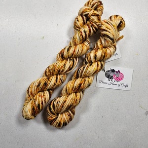May include: Two skeins of yarn in a brown, yellow, and orange colorway with a black stripe pattern. The yarn is labeled "Dina's Home of Crafts".