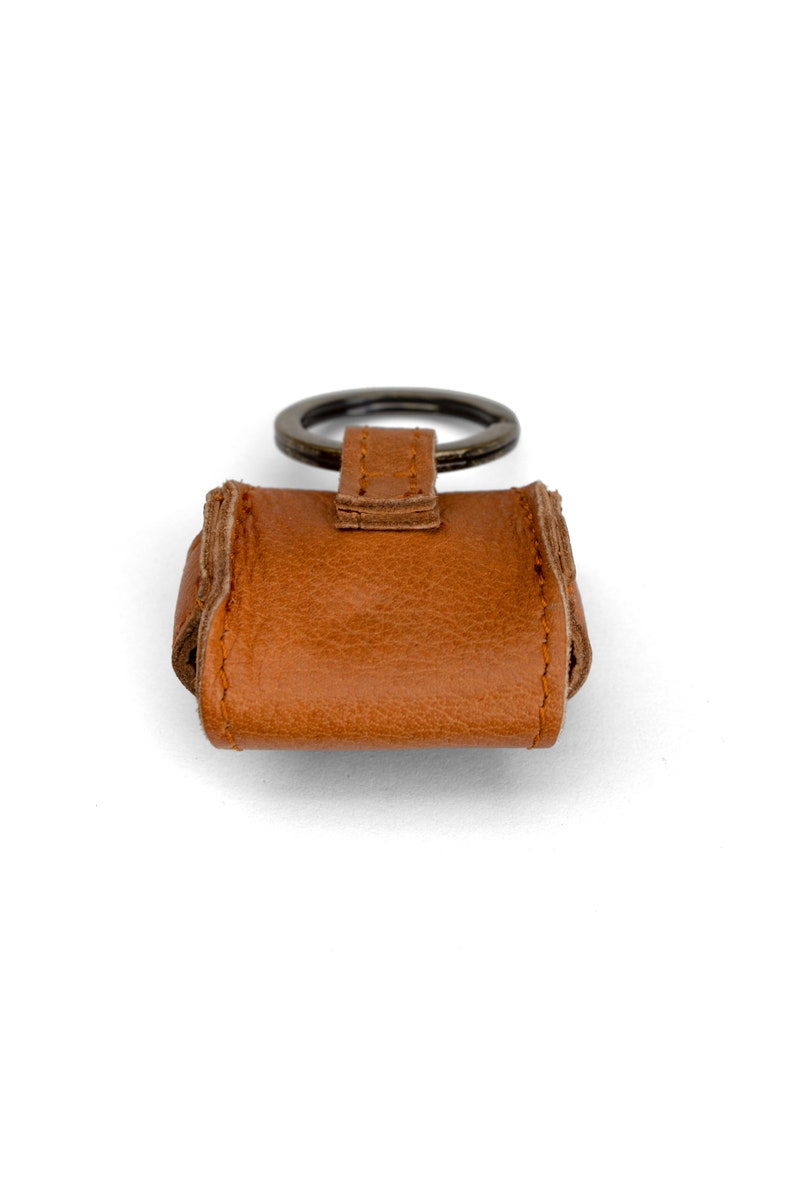 May include: A brown leather keychain with a metal ring. The keychain is designed to hold a small key or other item.