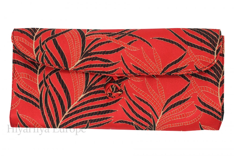 K&ouml;nnte beinhalten: Rote Clutch mit einem schwarzen und goldenen Palmenblatt-Muster. Die Clutch hat einen Klappverschluss mit einem Knopf.