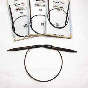 Peut inclure: Trois aiguilles à tricoter circulaires dans des emballages individuels. Les aiguilles sont brunes avec un cordon noir et sont étiquetées "Knit Pro Ginger" avec les tailles 3,25 mm, 3,00 mm et 2,75 mm. L'emballage indique également que les aiguilles mesurent 40,00 cm de long.