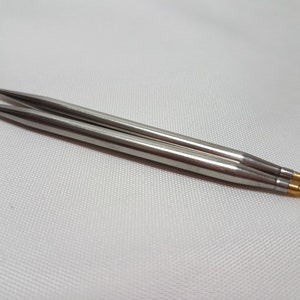 Puede incluir: Un par de agujas de tejer plateadas con puntas doradas.