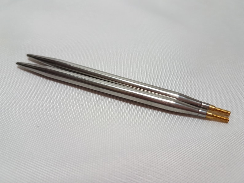 Puede incluir: Un par de agujas de tejer plateadas con puntas doradas.