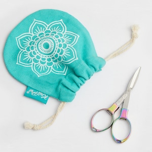 Pode incluir: Uma bolsa de cordão turquesa com um design de mandala branco e a palavra "KnitPro" impressa na parte inferior. Um par de pequenas tesouras arco-íris está ao lado da bolsa.
