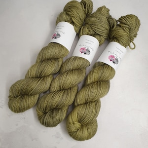 Könnte beinhalten: Drei Knäuel grünes Garn mit weißen Etiketten, auf denen "Two of a Kind" und "100% Superwash Merino Wool" steht.