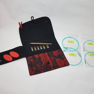 Puede incluir: Una funda de tela negra y roja con cierre de cremallera, que contiene un juego de agujas de tejer y un juego de cuatro agujas circulares. Las agujas circulares son turquesa y est&aacute;n empaquetadas en bolsas de pl&aacute;stico transparentes.