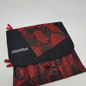 Puede incluir: Bolsa de tela negra con un patr&oacute;n de rosas rojas y el texto "HiyahHiya" bordado en la parte delantera.